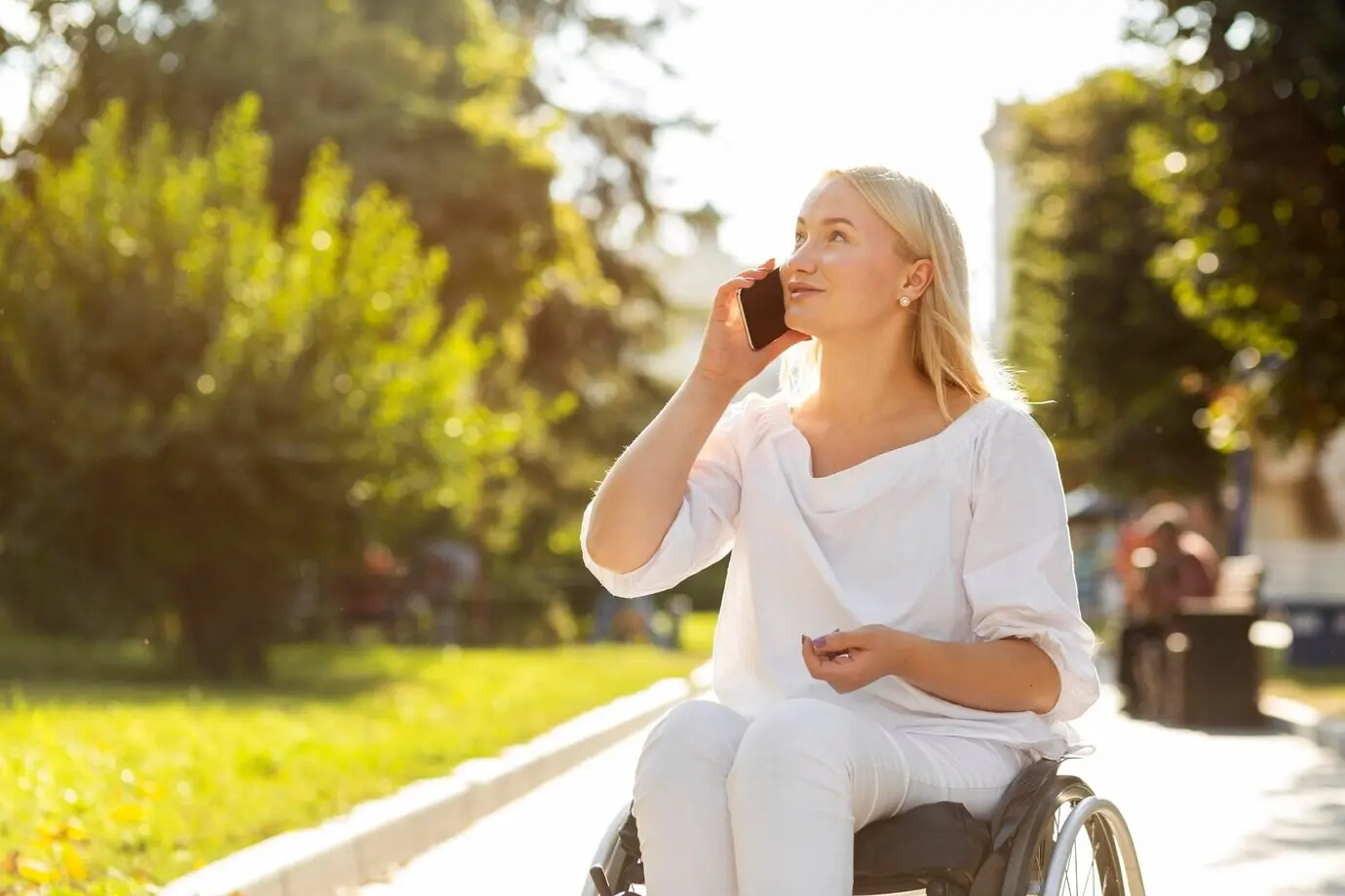 A woman in a wheelchair is talking on the phone outside.