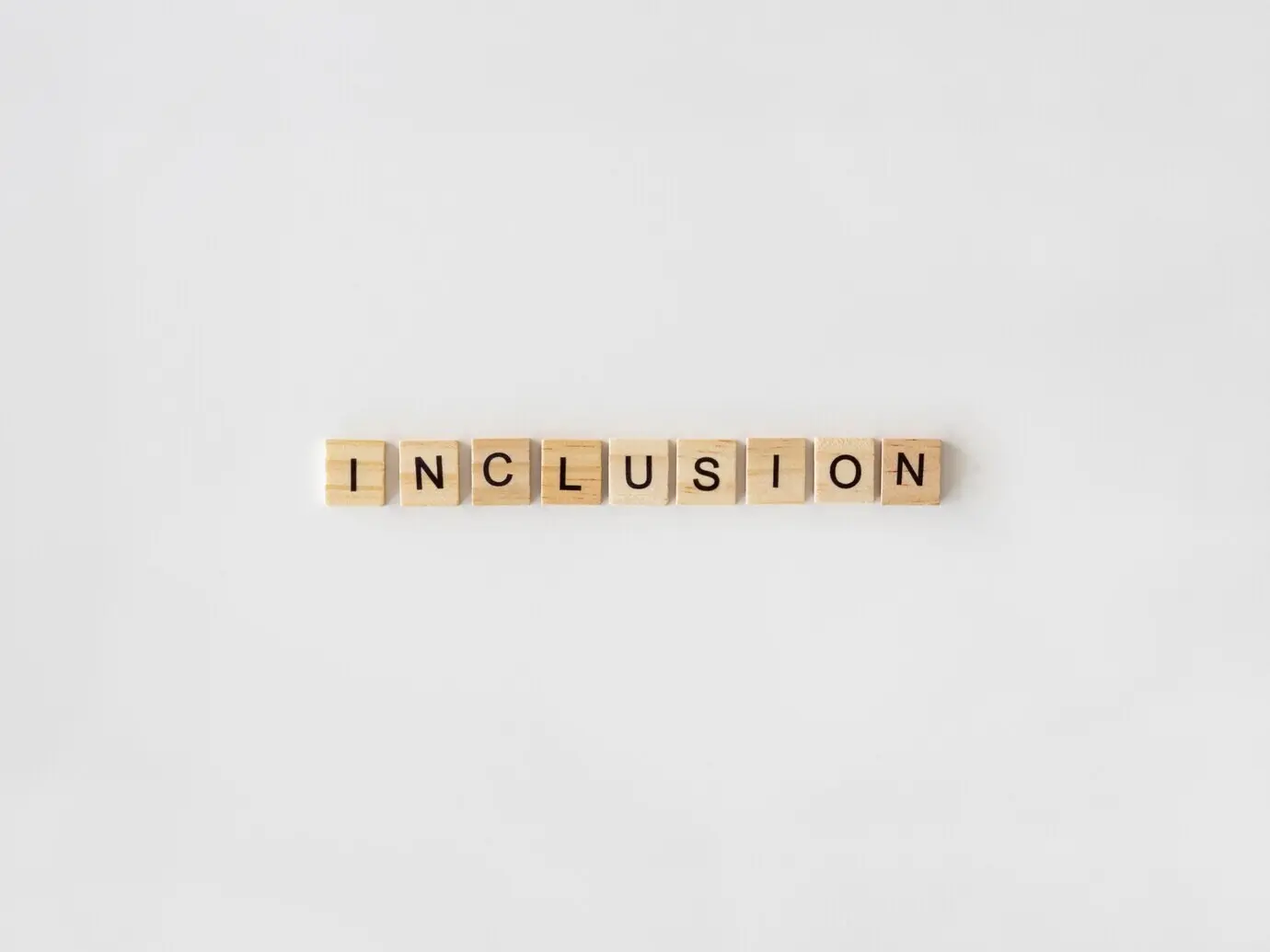 The word “Inclusion” spelled with Scrabble letters on a white background.